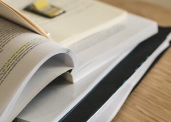 A close-up of a stack of open and closed books and documents on a wooden surface, with highlighted text visible and a paperclip on top. | MyBestHub.com