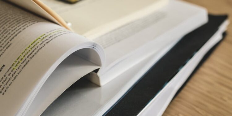 A close-up of a stack of open and closed books and documents on a wooden surface, with highlighted text visible and a paperclip on top. | MyBestHub.com