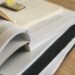 A close-up of a stack of open and closed books and documents on a wooden surface, with highlighted text visible and a paperclip on top. | MyBestHub.com